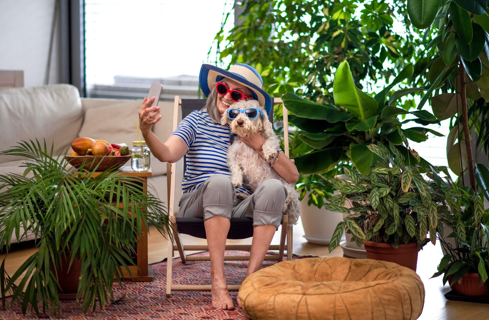 Older woman takes a selfie at home with her dog, both wearing sunglasses.