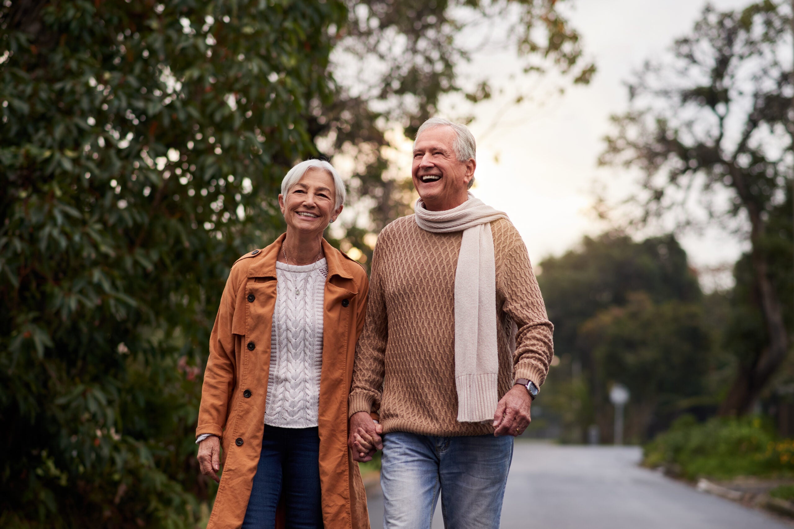 Older couple holding hands while walking outdoors on a quiet neighborhood street in cool weather