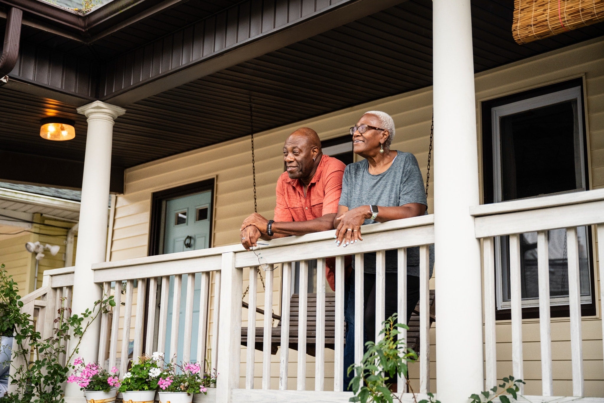 A couple standing together on a front porch, leaning on the railing and smiling.