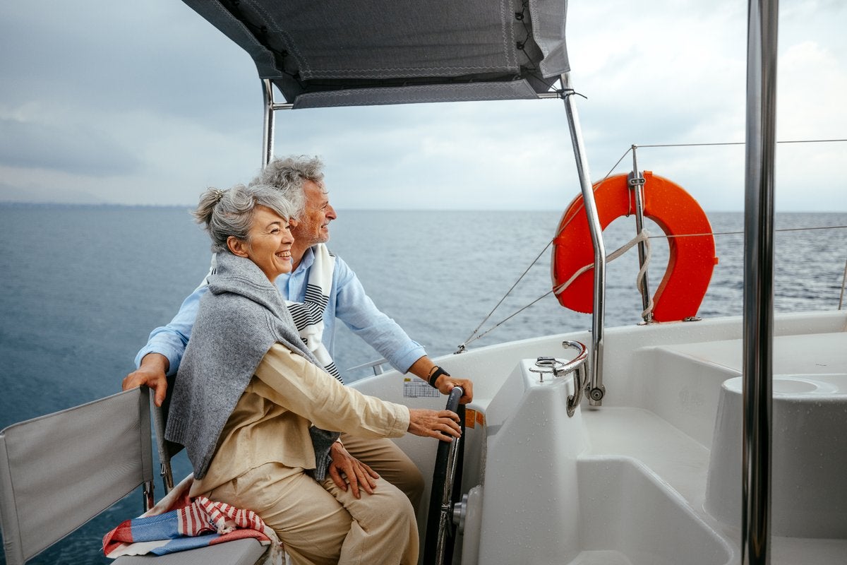 Older couple smiling together while sailing on a boat and looking toward the horizon.