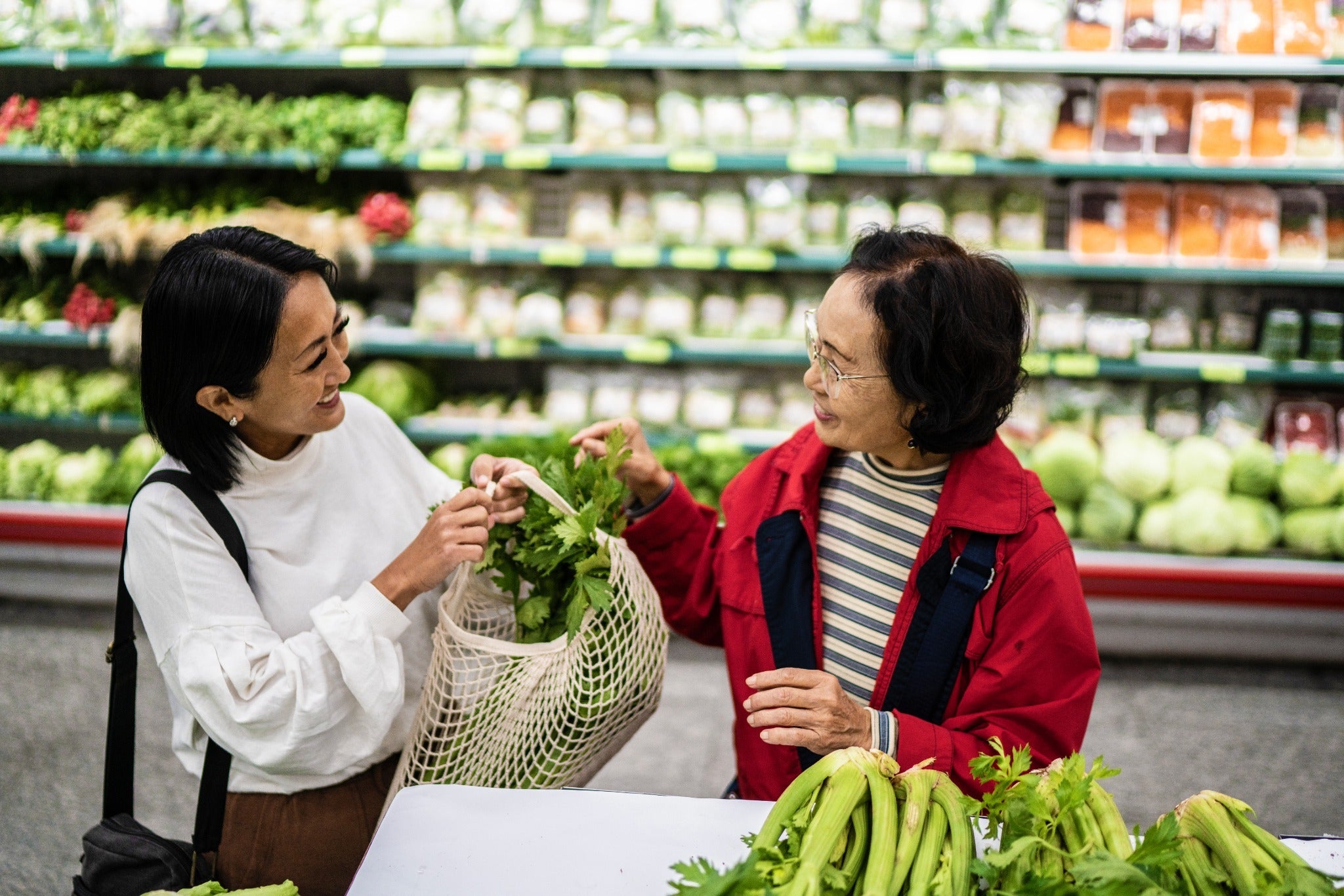 Adult daughter and her aging mother shopping for fresh produce together at a grocery store.