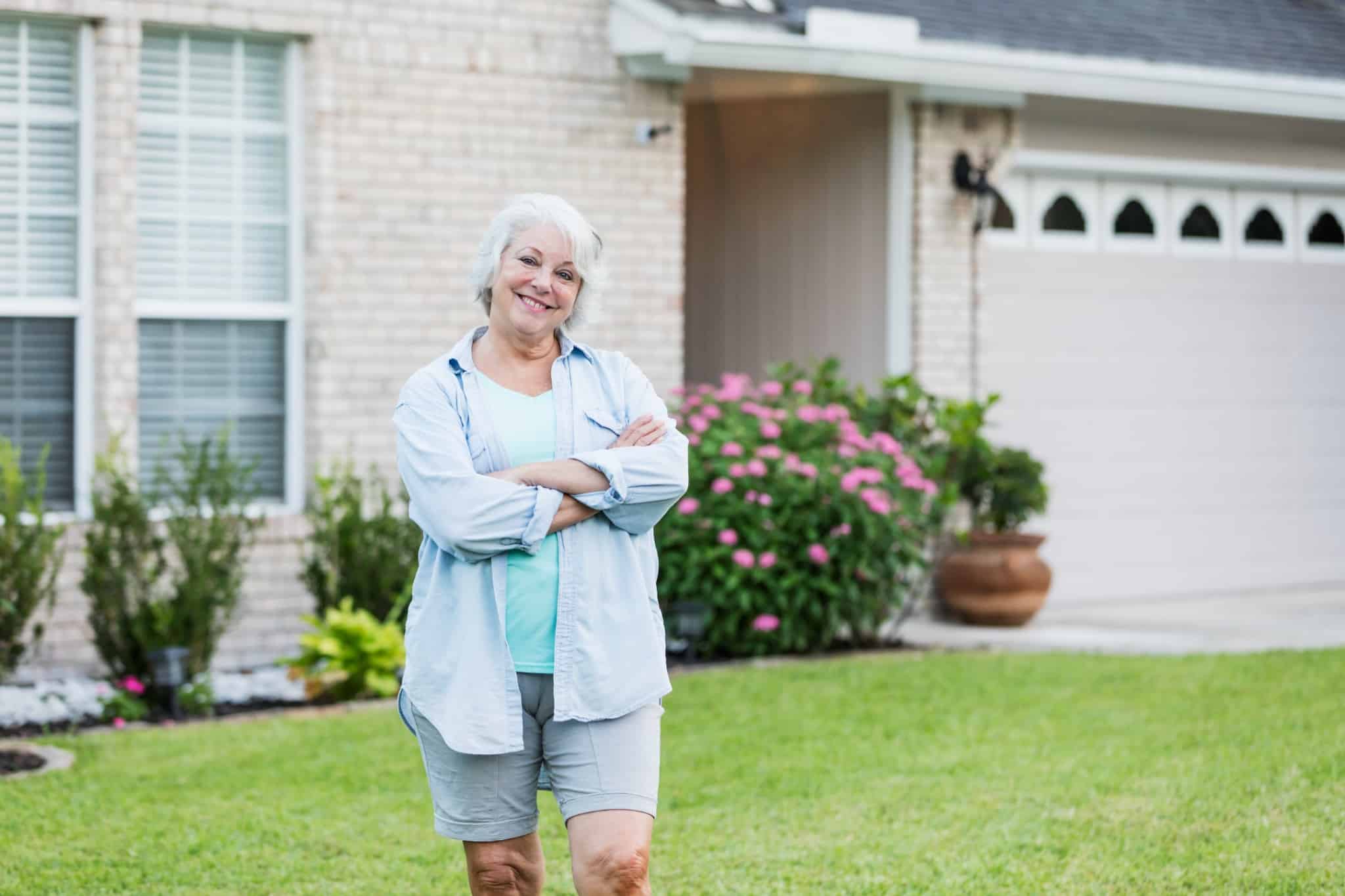 Older woman standing confidently in front of her home, representing homeownership and access to home equity