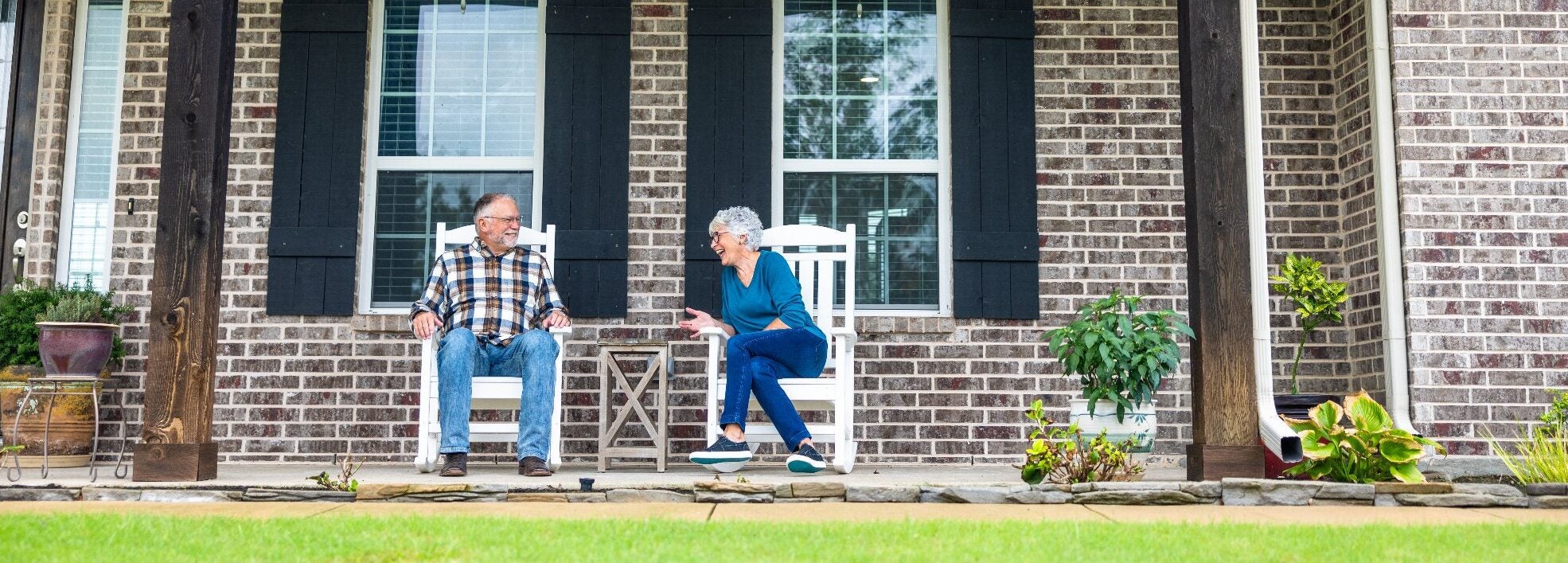 Older couple sitting on their front porch talking outside their brick home